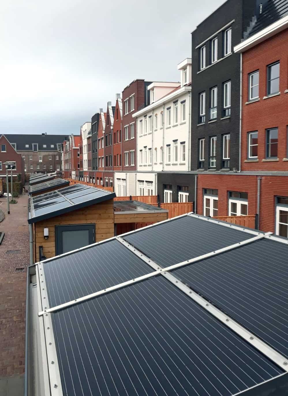 Een straat met verschillende kleuren bakstenen huizen met bergingen in de tuin van hout met zonnepanelen op het dak