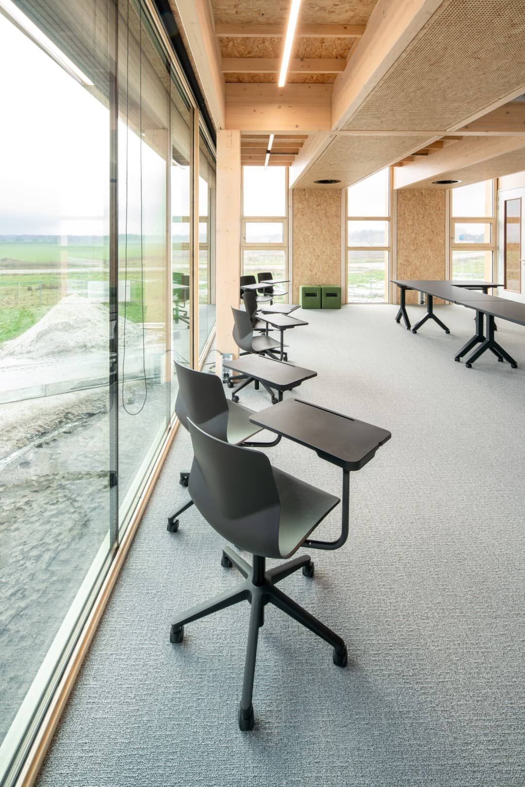 Ruimte met zwarte stoelen met een bureau eraan vast met grote ramen links