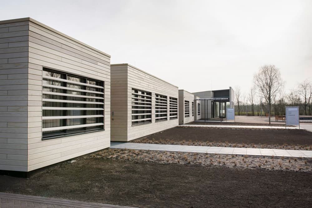 Vierkante gebouwen van wit hout met paden van tegels tussen het zand