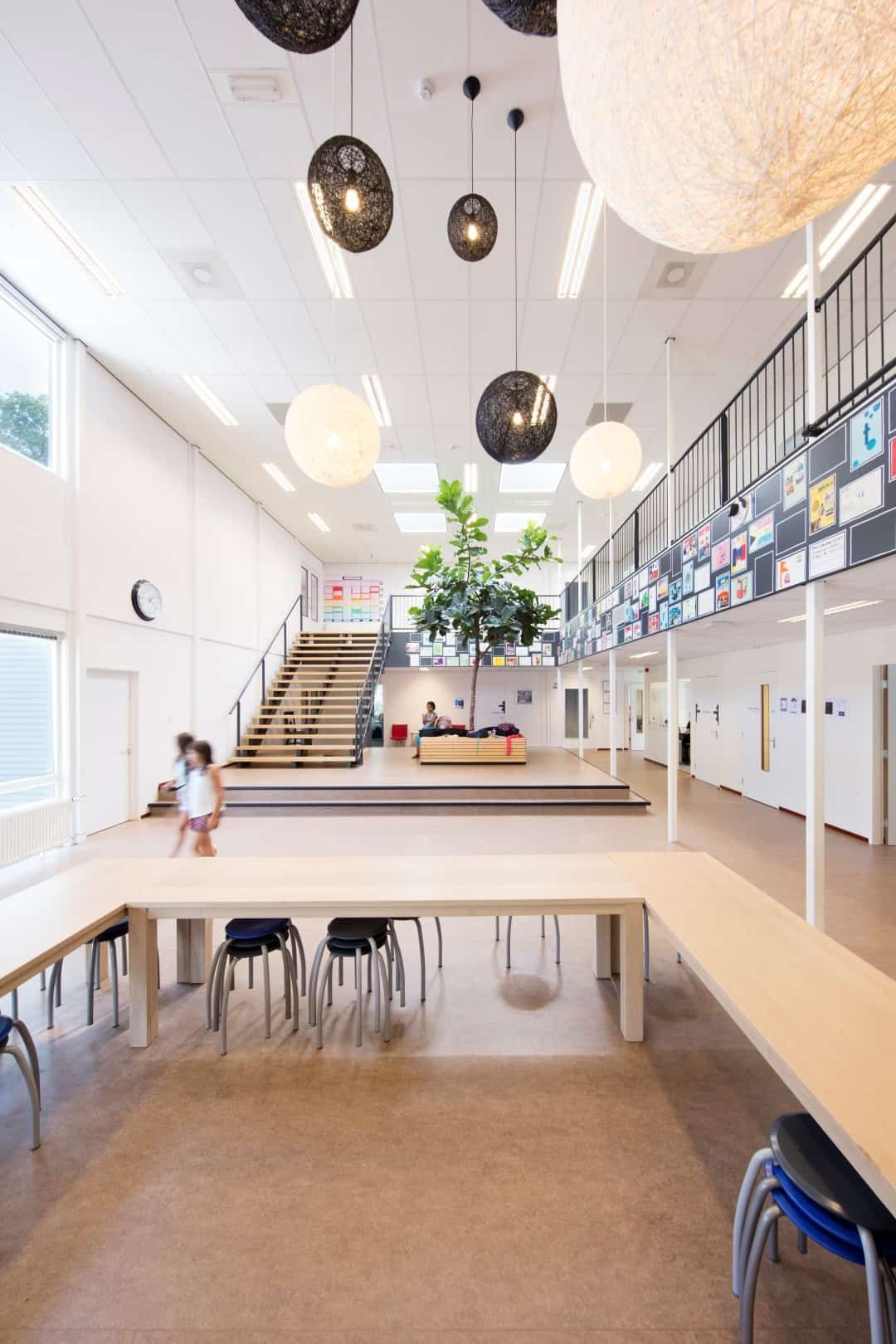 De binnenkant hal van de Internationale school in Utrecht met veel ronde lampen en lichte kleuren.