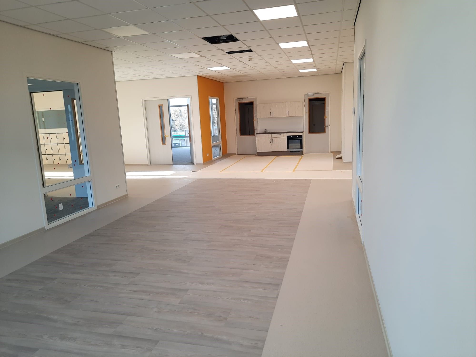 Witte binnenkant met ene oranje muur van een gebouw met een houten vloer en een keuken aan de achterwand