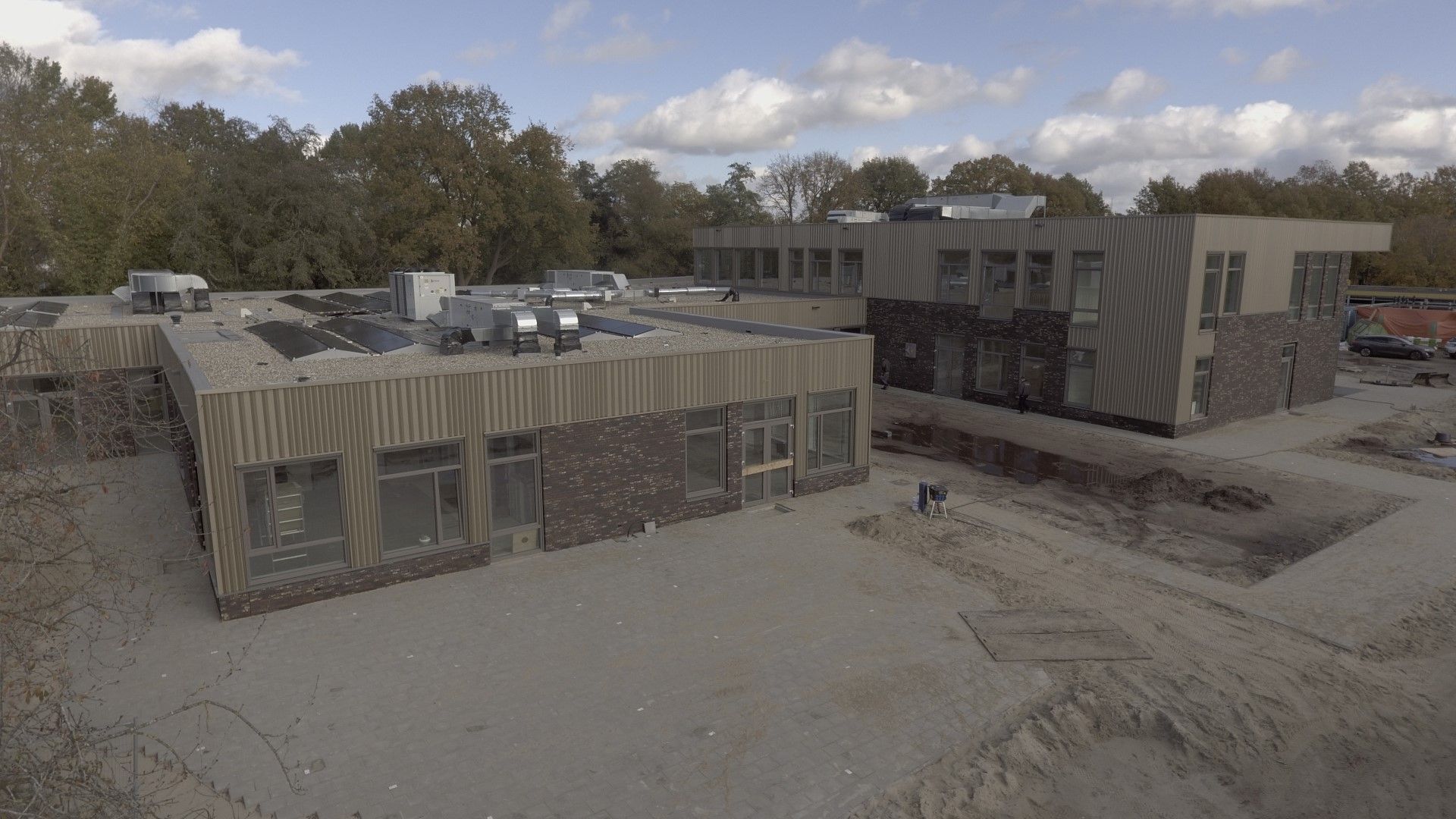 Houten gebouw in aanbouw op een zandvlakte met bomen erachter