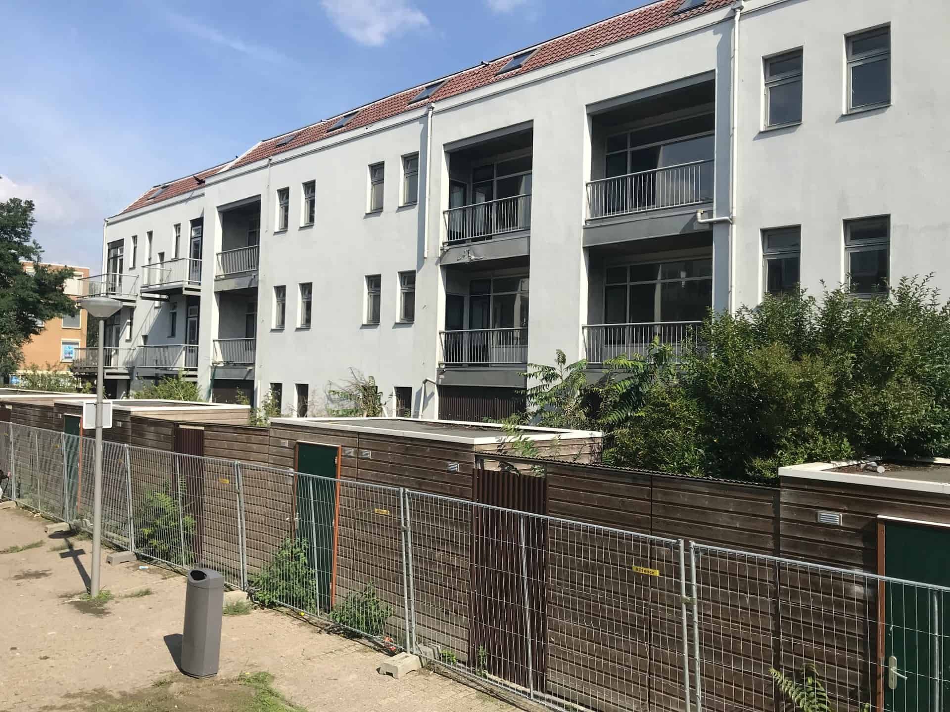 Wit flatgebouw met houten tuinhuisjes en hekken ervoor