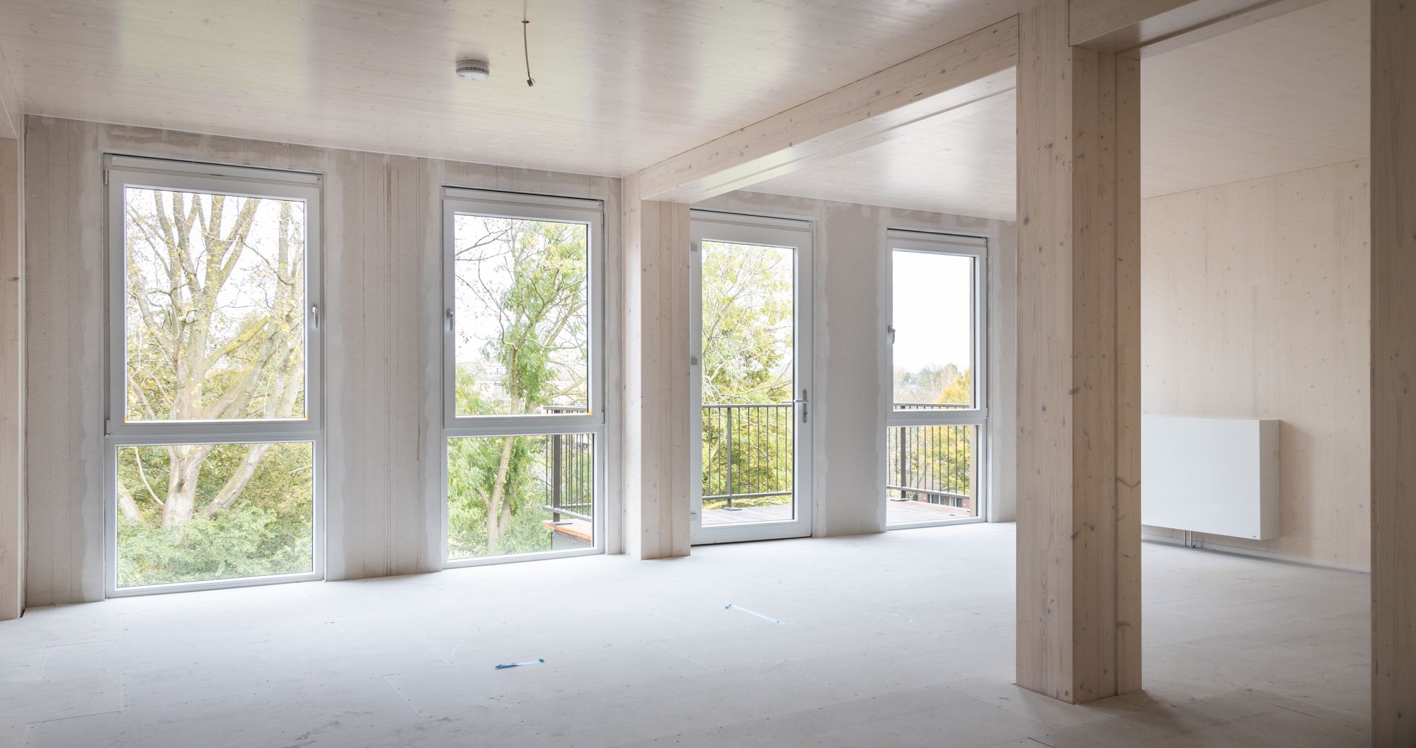 Binnenkant van een leeg appartement met balkon, houten balken en uitzicht op bomen