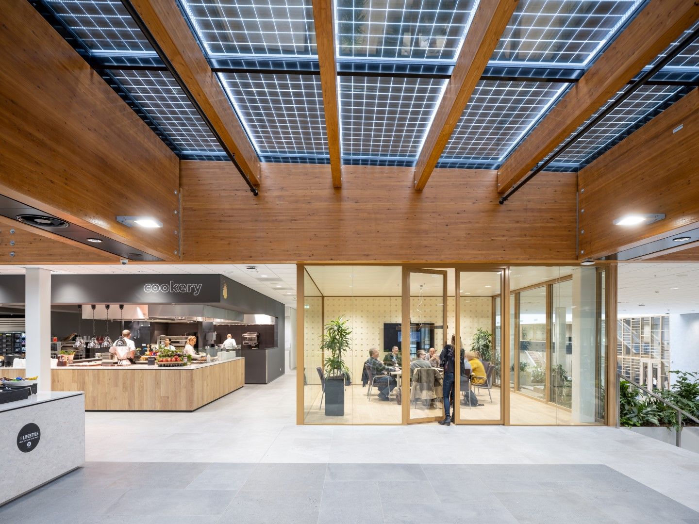 De kantine met houten en glazen plafond met een keuken en glazen ruimte met een tafel en mensen erin