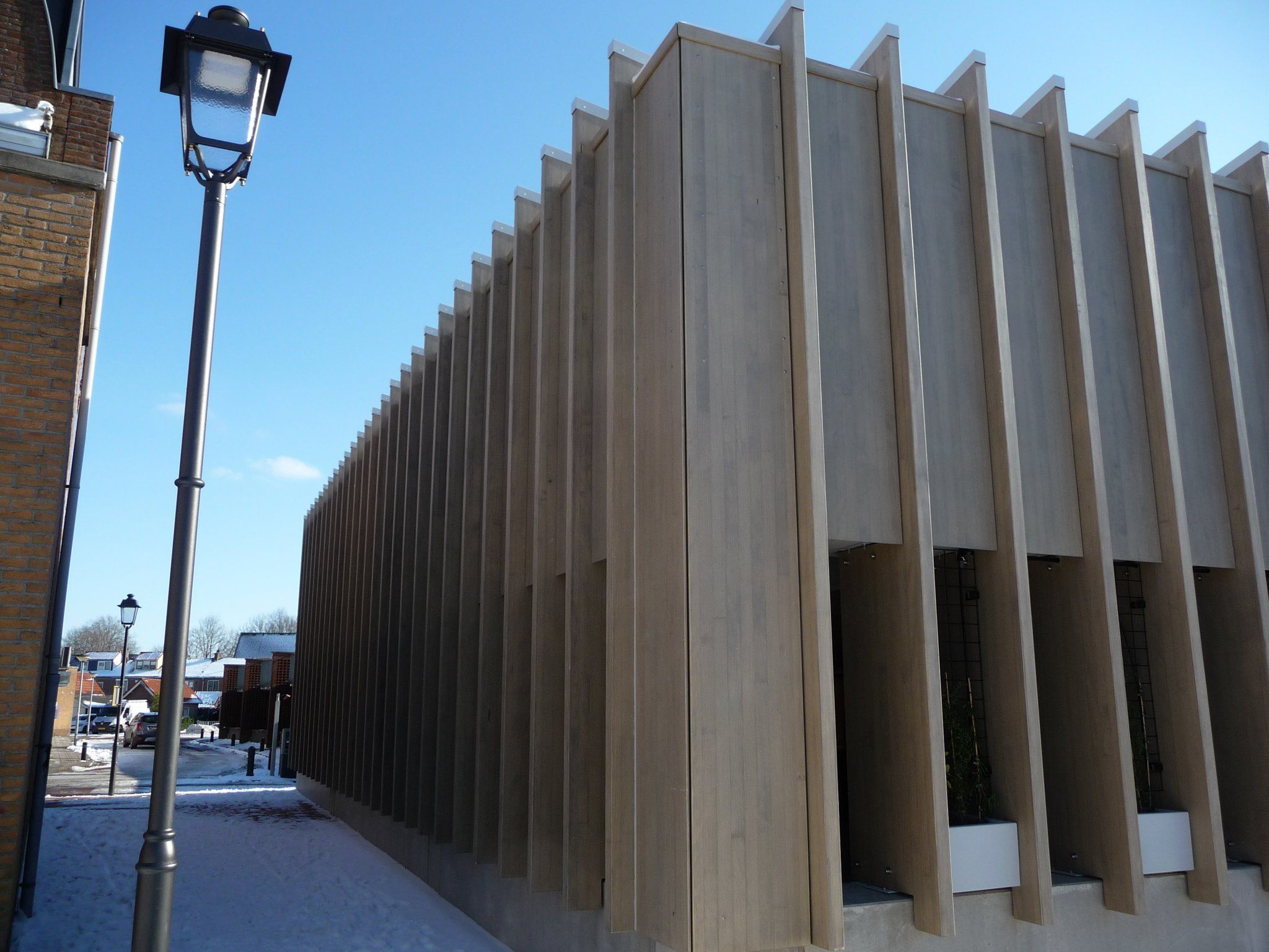 Hoek van een houten gebouw met langwerpige gaten aan de onderkant en lantaarnpaal