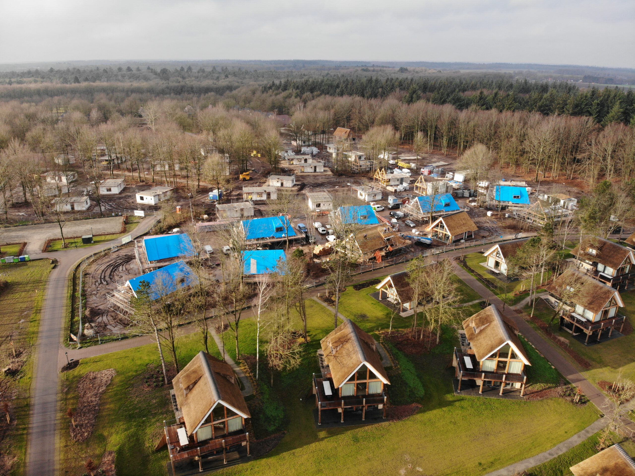 Een vakantiepark van bovenaf met rieten daken en daken in aanbouw in de natuur