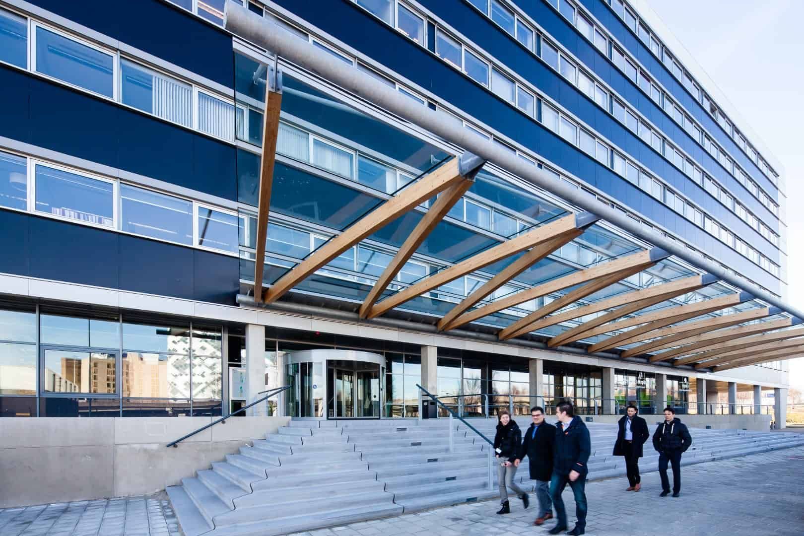 Voorkant met trap van een glazen gebouw met glazen overkapping rustend op houten balken
