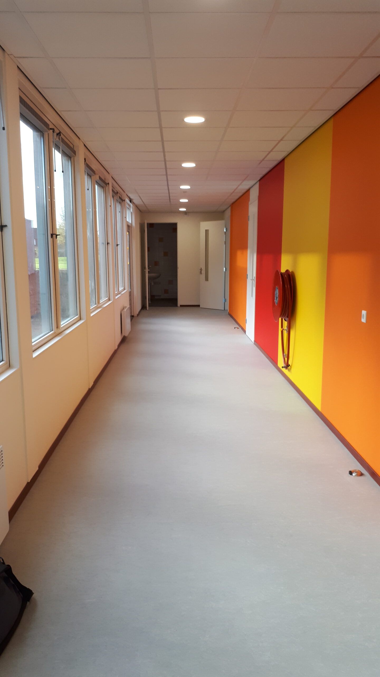 De gang met oranje, rode en gele muur van de tijdelijke huisvesting van de school in Dronten