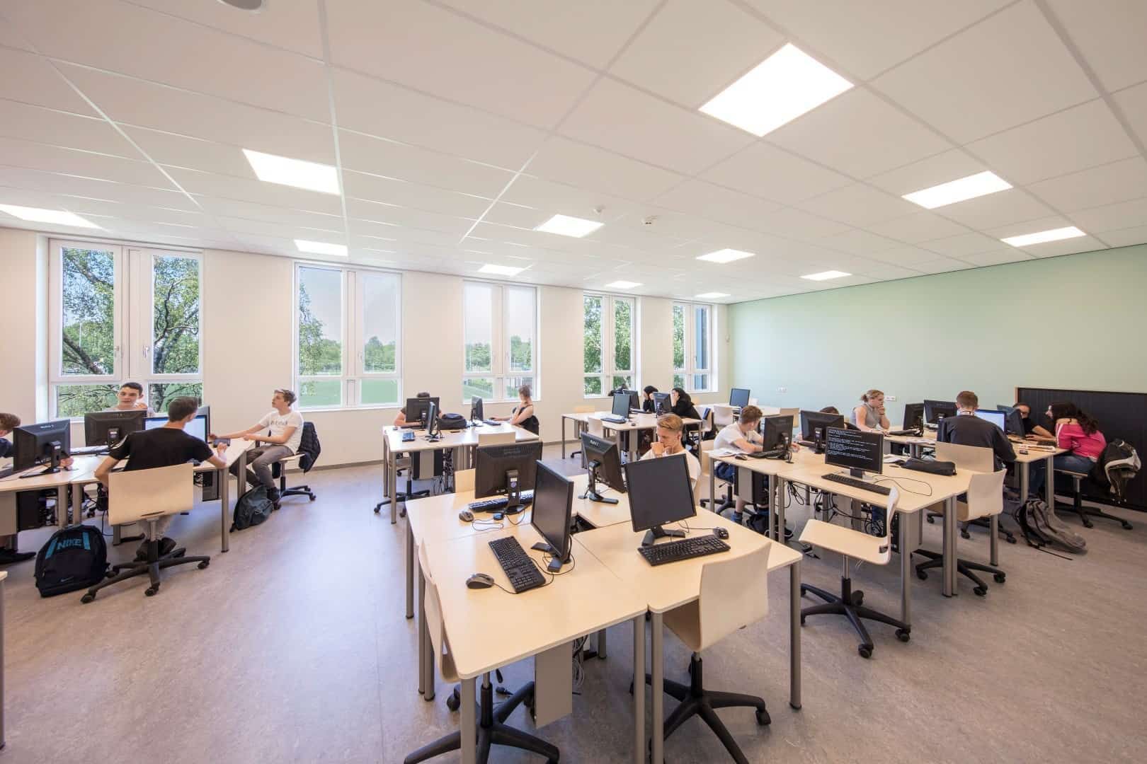 Computerlokaal met een groene muur en licht meubilair en leerlingen
