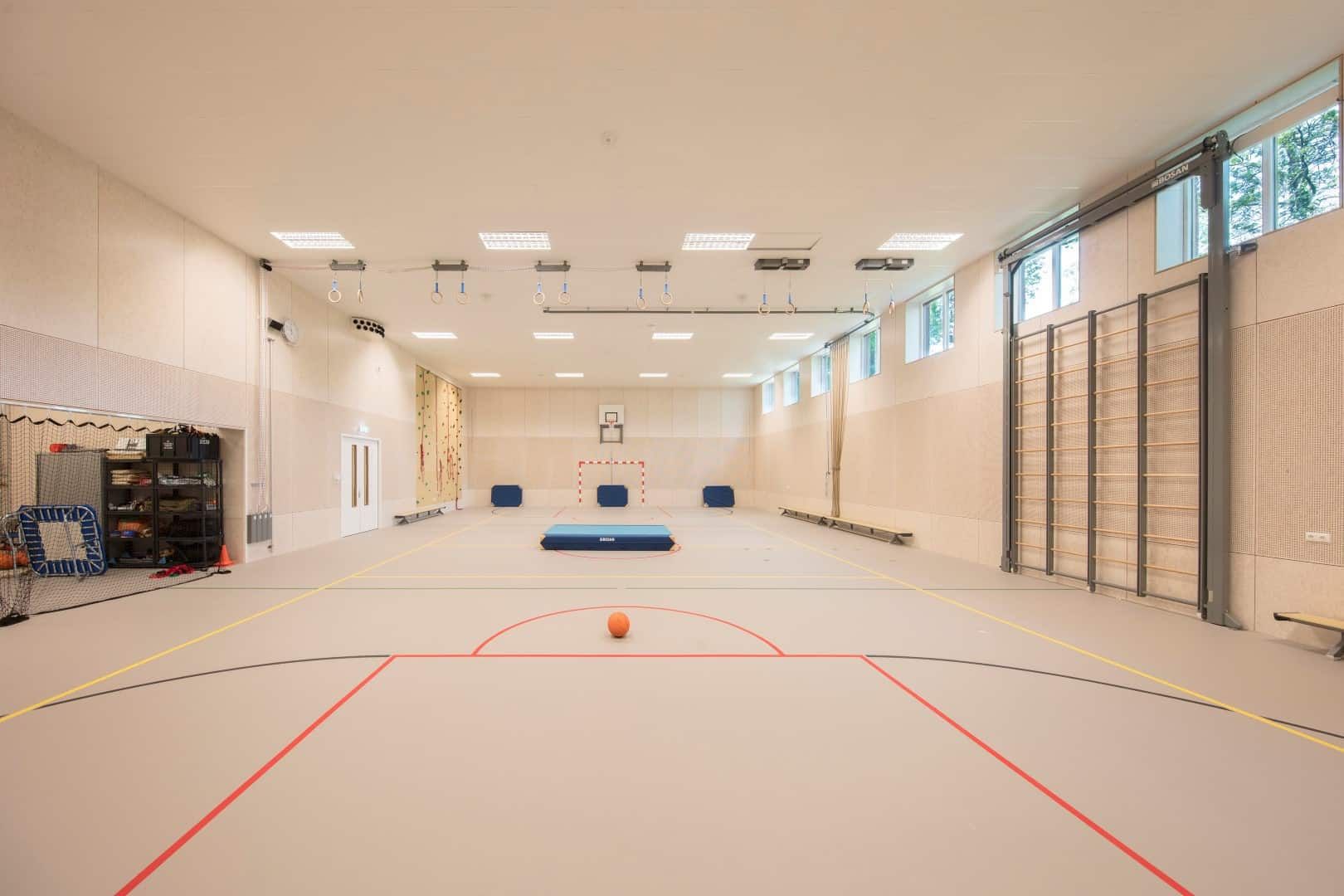 De sportzaal van het Wellantcollege met lichte kleuren, strepen op de grond, sportattributen en een opberghok links