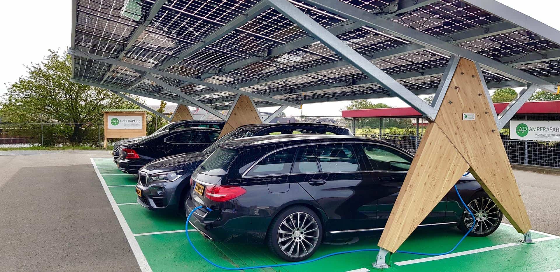 Overkapping voor auto's van houten palen met zonnepanelen erop met auto's eronder op groen asfalt