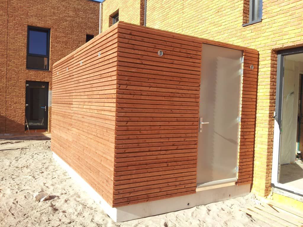 Houten berging met beige deur aan een huis vast op zand