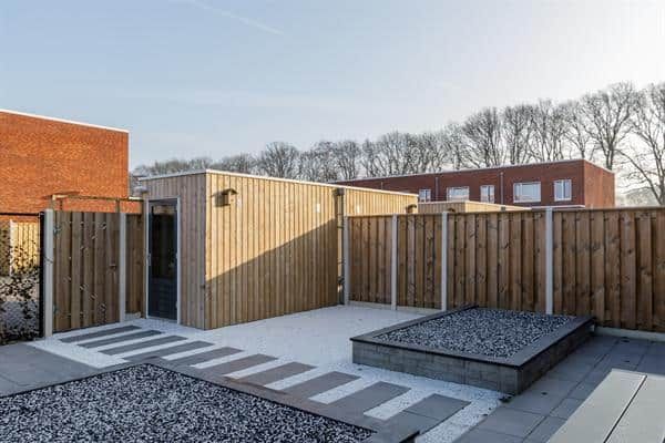 Betegelde tuin met grijs grind en een houten schutting met houten schuurtje met plat dak