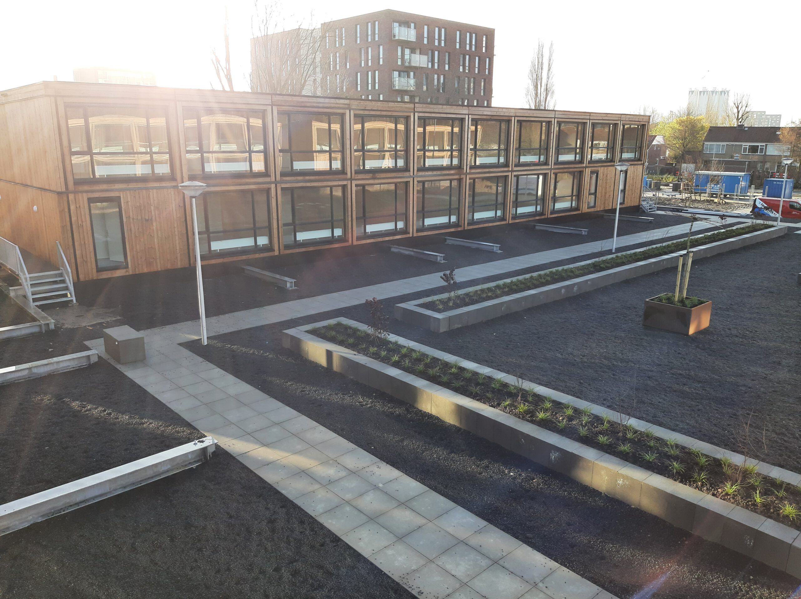 Houten gebouw met grote ramen met een tuin aan grind, langwerpige plantenbakken en een pad van stoeptegels