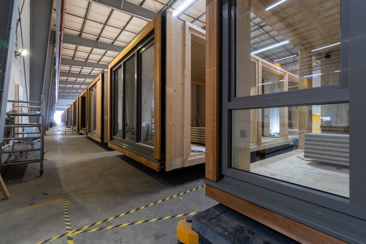 Houten woonmodules met grote ramen en zwarte kozijnen in een fabriek