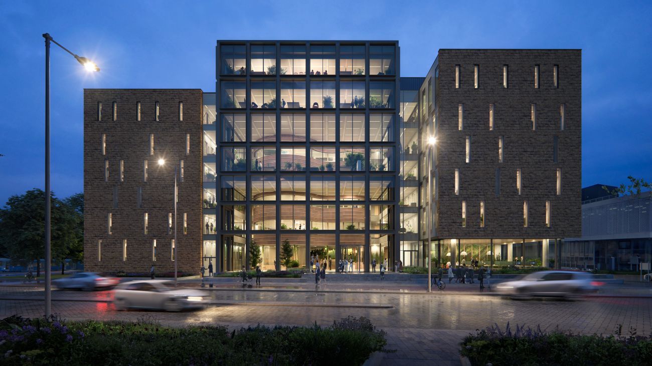 Groot gebouw met lichte bakstenen aan de zijkanten en grote ramen in het middelste gedeelte aan een drukke weg met een trap naar de weg toe en veel planten