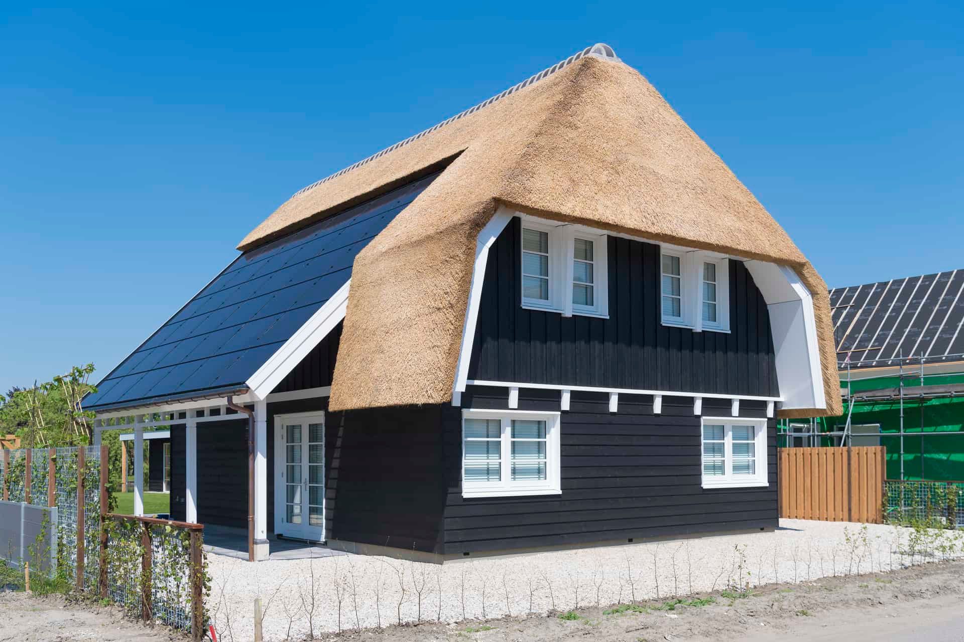 Zwart, houten huis met rieten kap en zonnepanelen