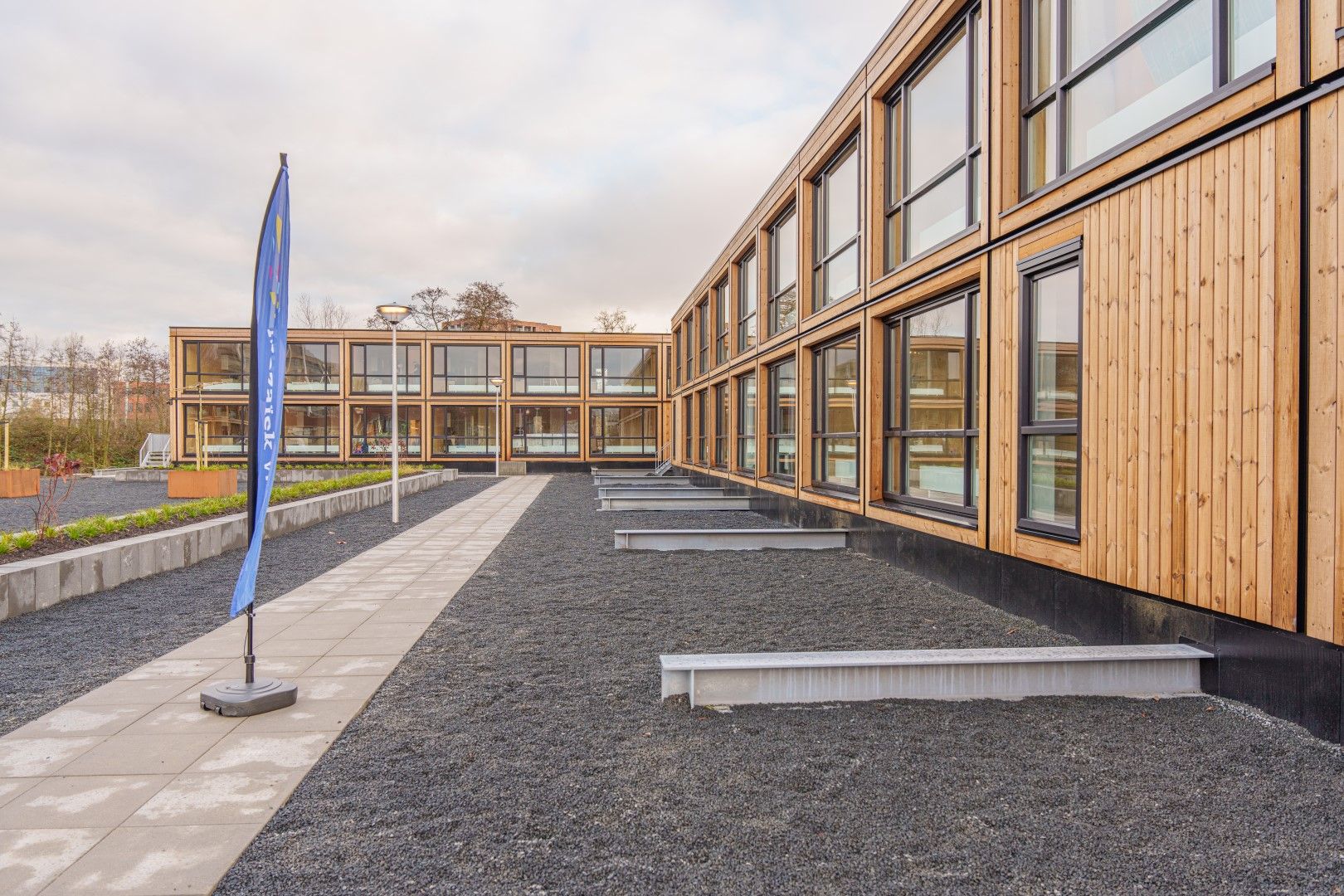 Houten woongebouwen met een pad met een vlag erop en en groenstrook en zandstrook