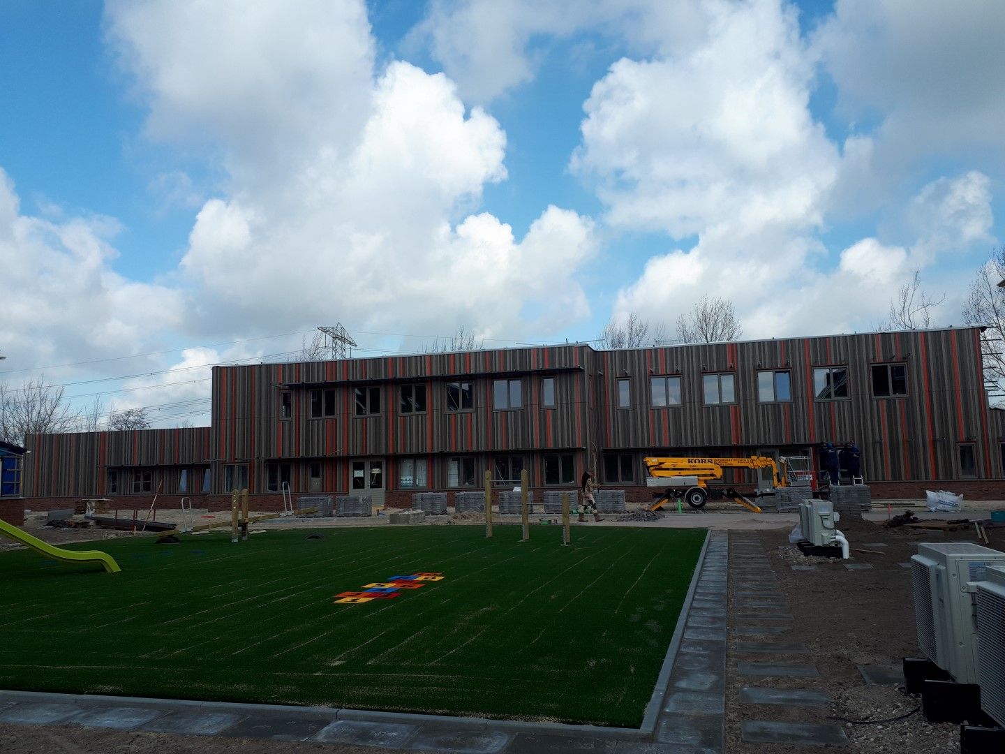 Rechthoekig gebouw met bruin en rode strepen met een grasveld ervoor
