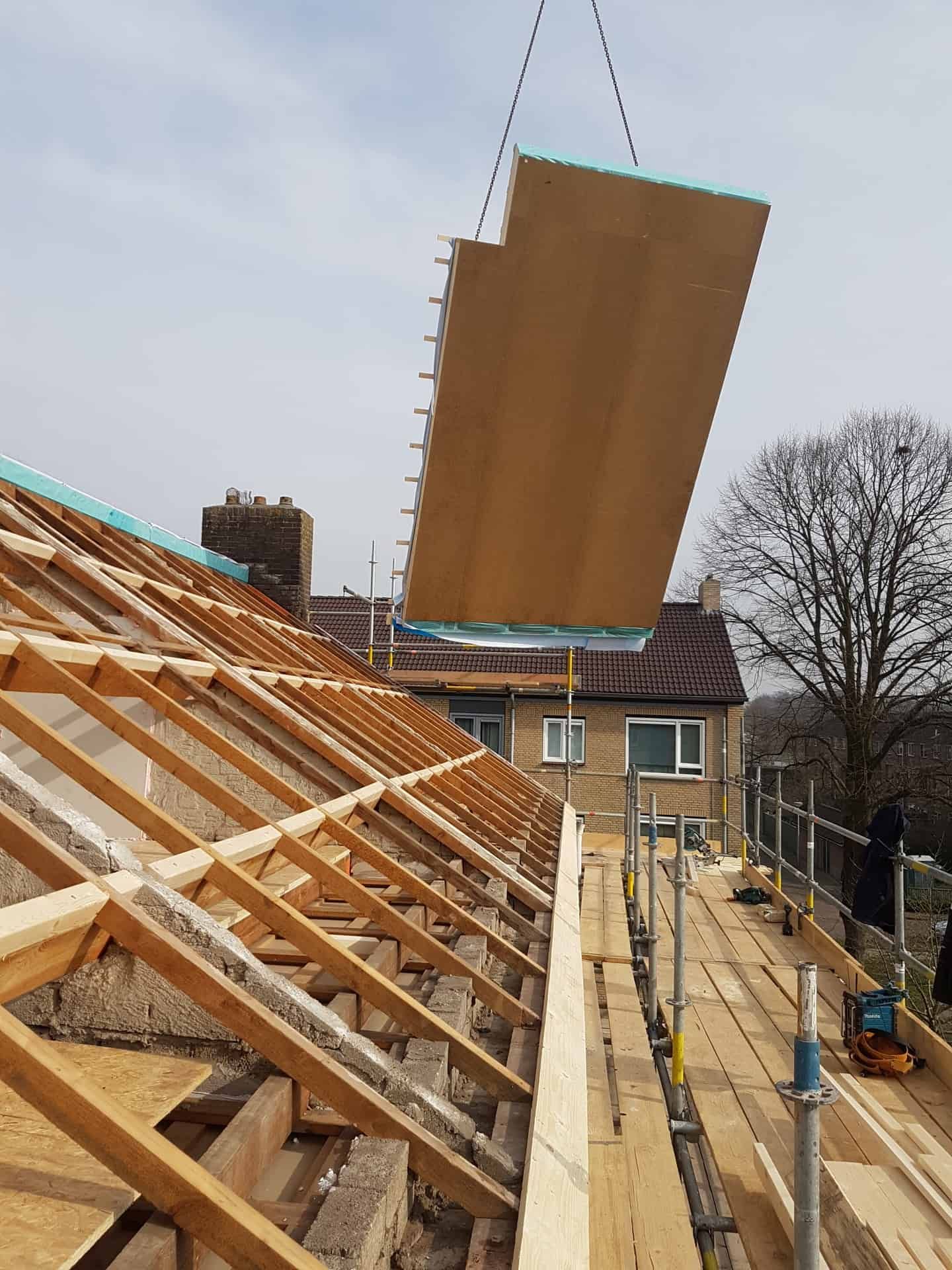 Een houten dak in aanbouw met een houten plaat aan een hijskraan