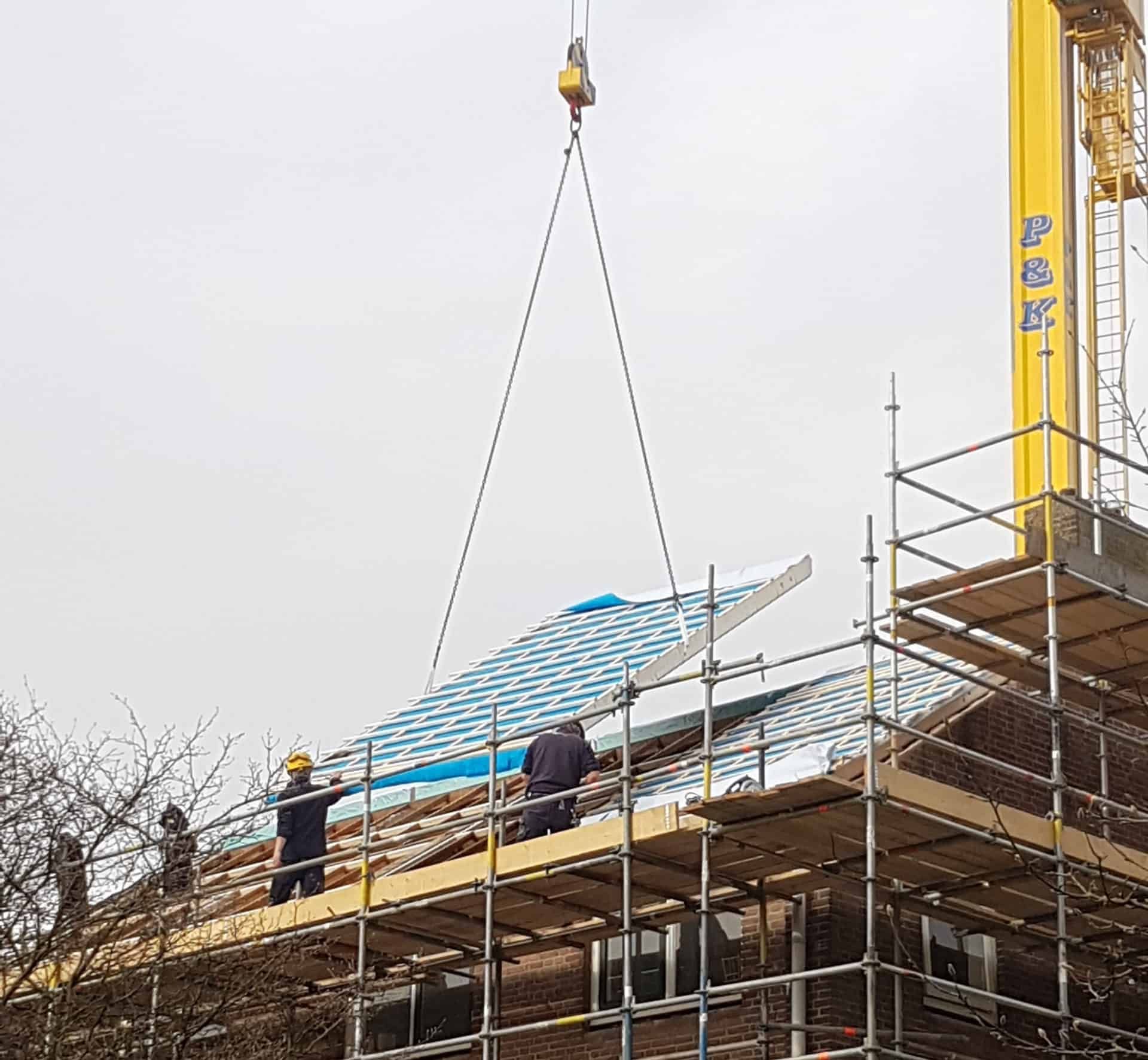 Een huis in aanbouw met een blauwe dakplaat aan een hijskraan