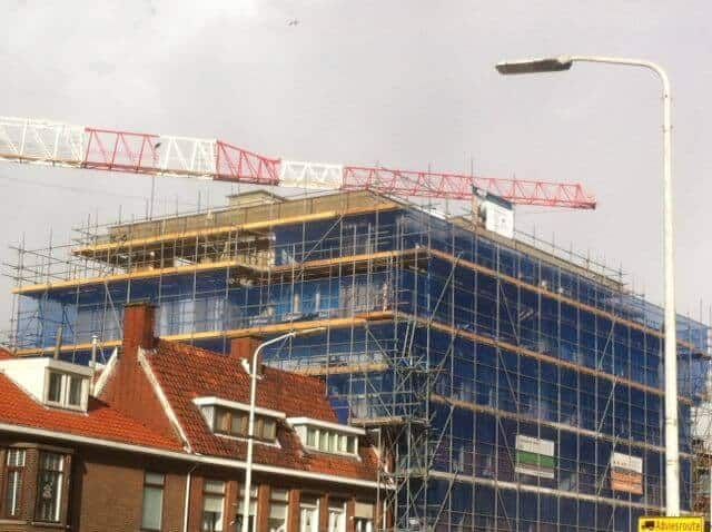 Een appartementencomplex in aanbouw met hekken eromheen en een rood met witte hijskraan