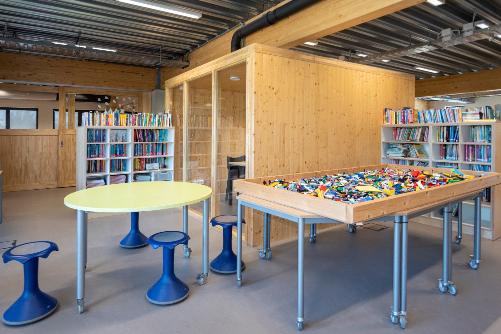 Houten bak met lego, houten boekenkasten en een houten hok met ramen met zitplekken
