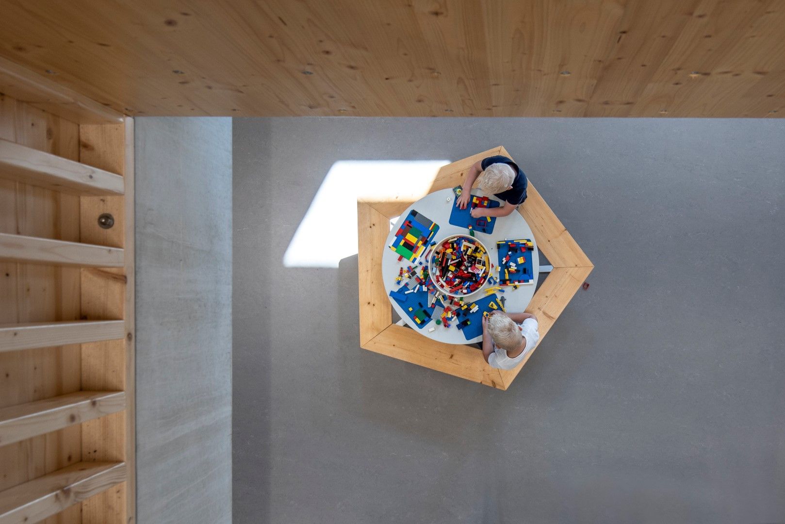 Een ronde tafel met houten banken en twee spelende kinderen met lego op de bankjes vanaf boven