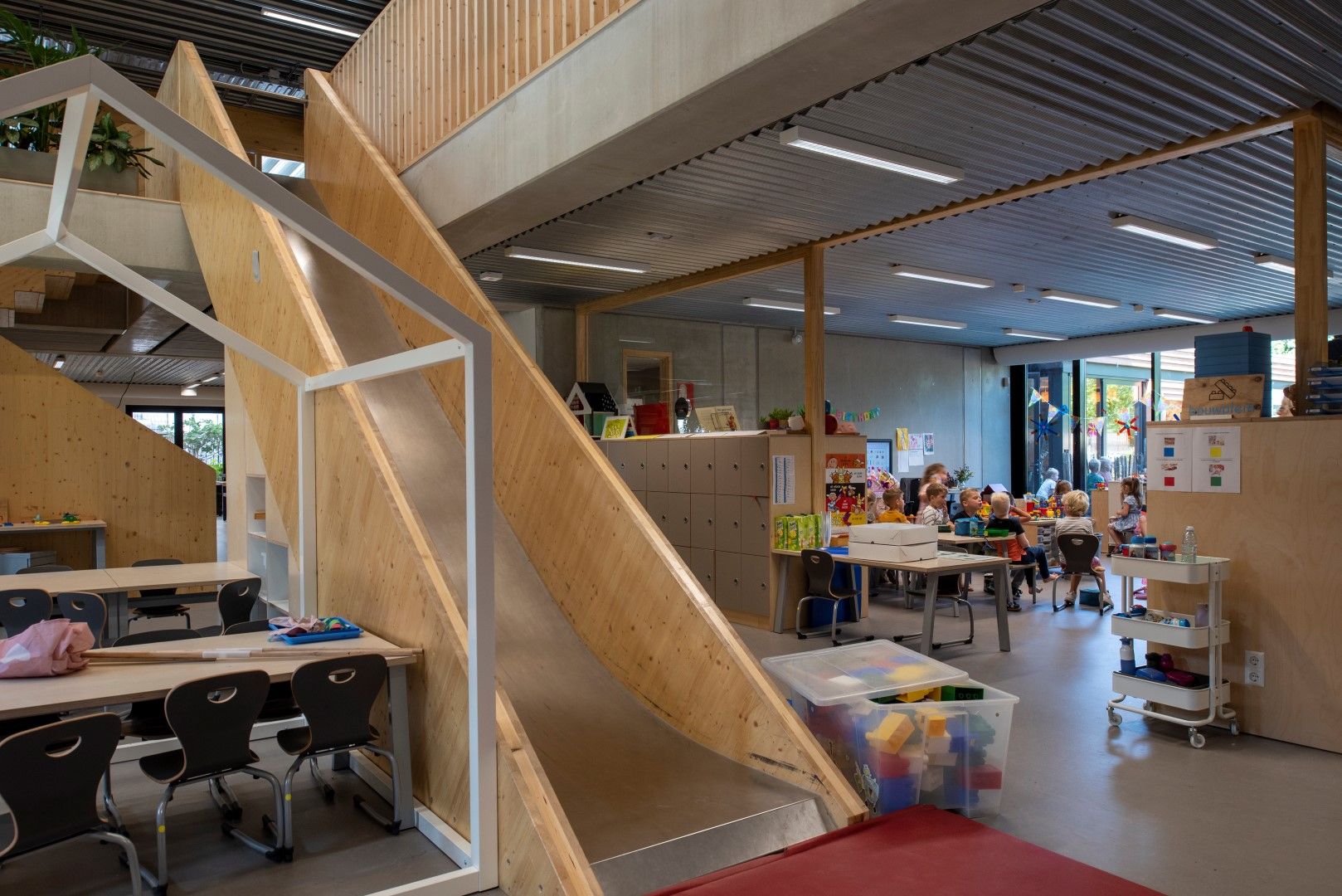 Glijbaan vanaf de bovenverdieping met daarachter een klaslokaal met kinderen