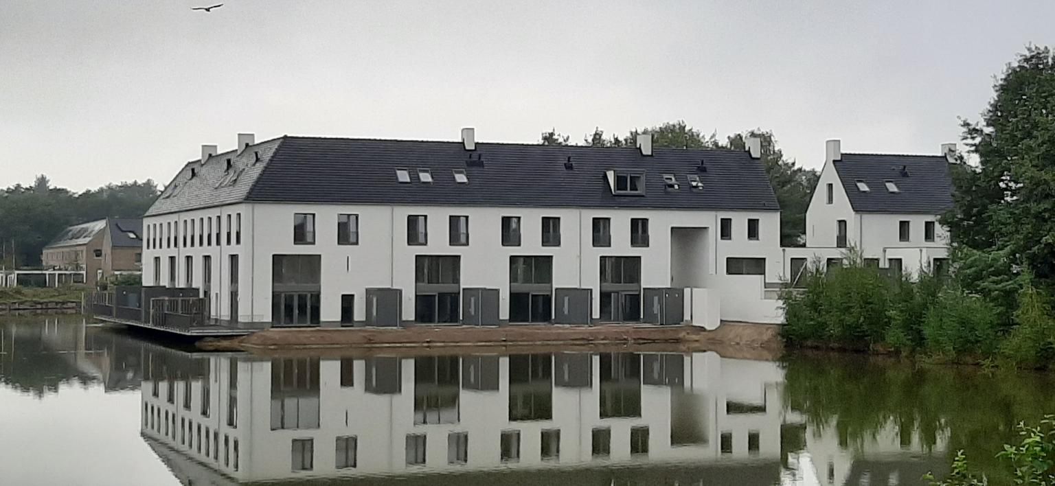 Witte rijtjeshuizen aan het water met grijze schuurtjes op zand