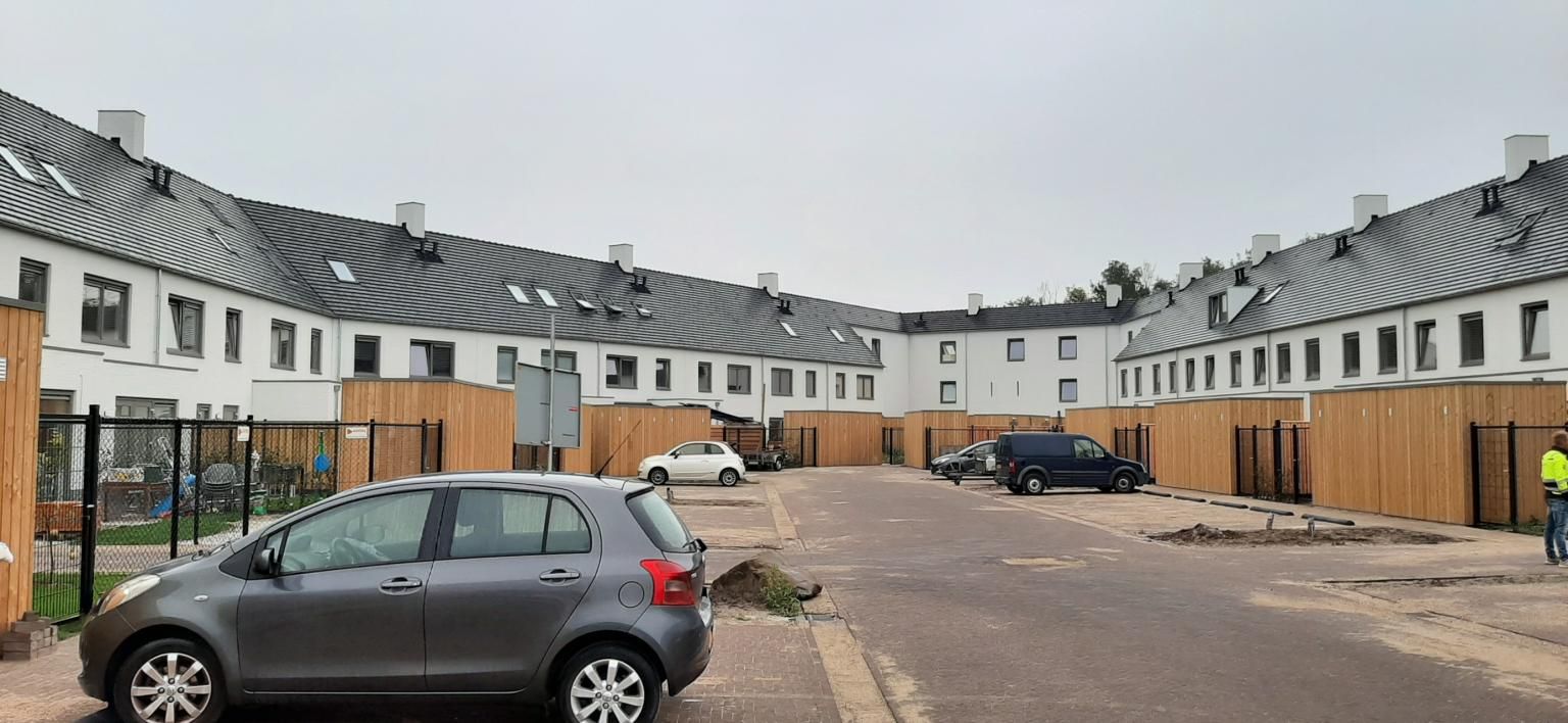 Witte rijtjeshuizen in een woonwijk met houten schuurtjes grenzend aan een parkeerplaats