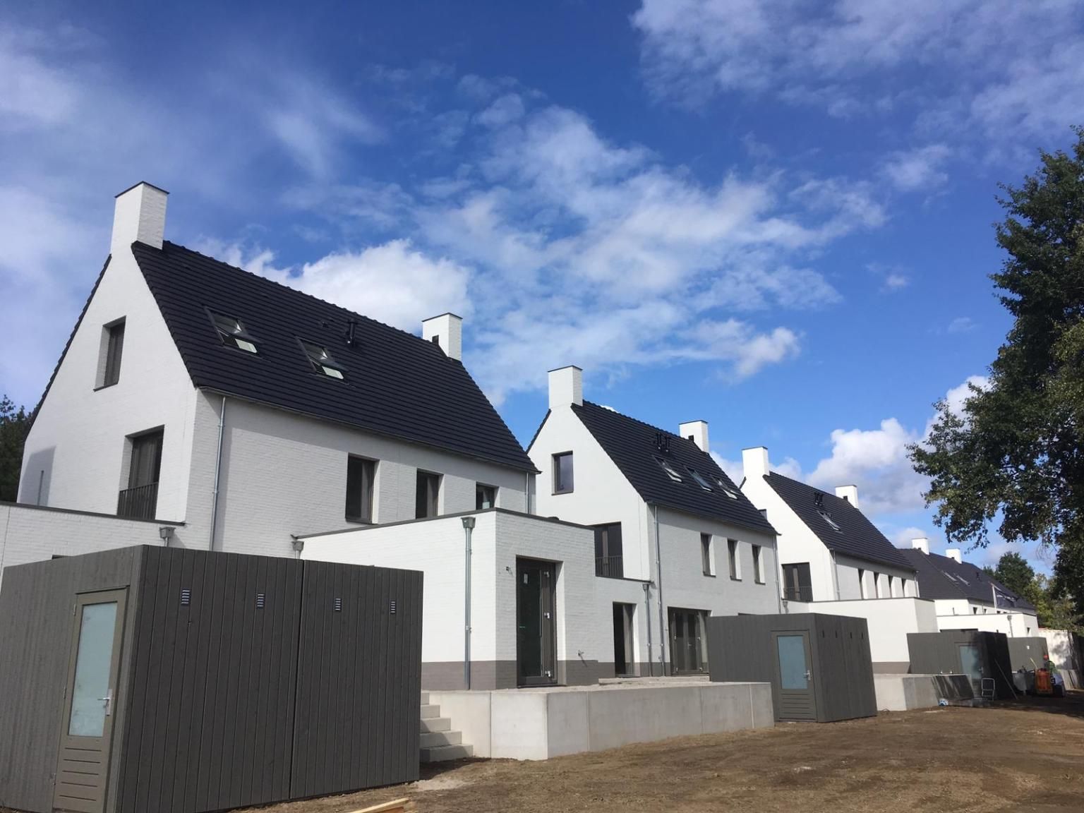 Witte twee-onder-een-kap huizen met zwart dak, grijze houten schuurtjes en een trappetje naar zand