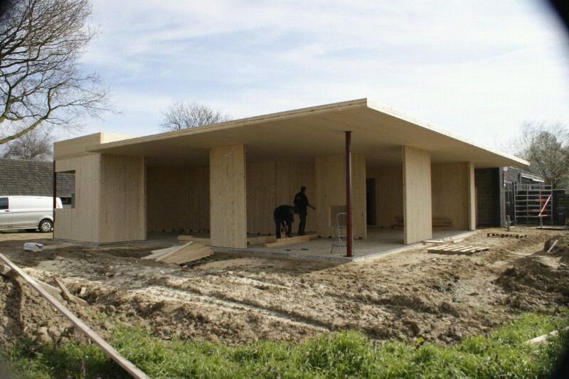 Houten gebouw op zand en gras waar twee mensen aan het werk zijn