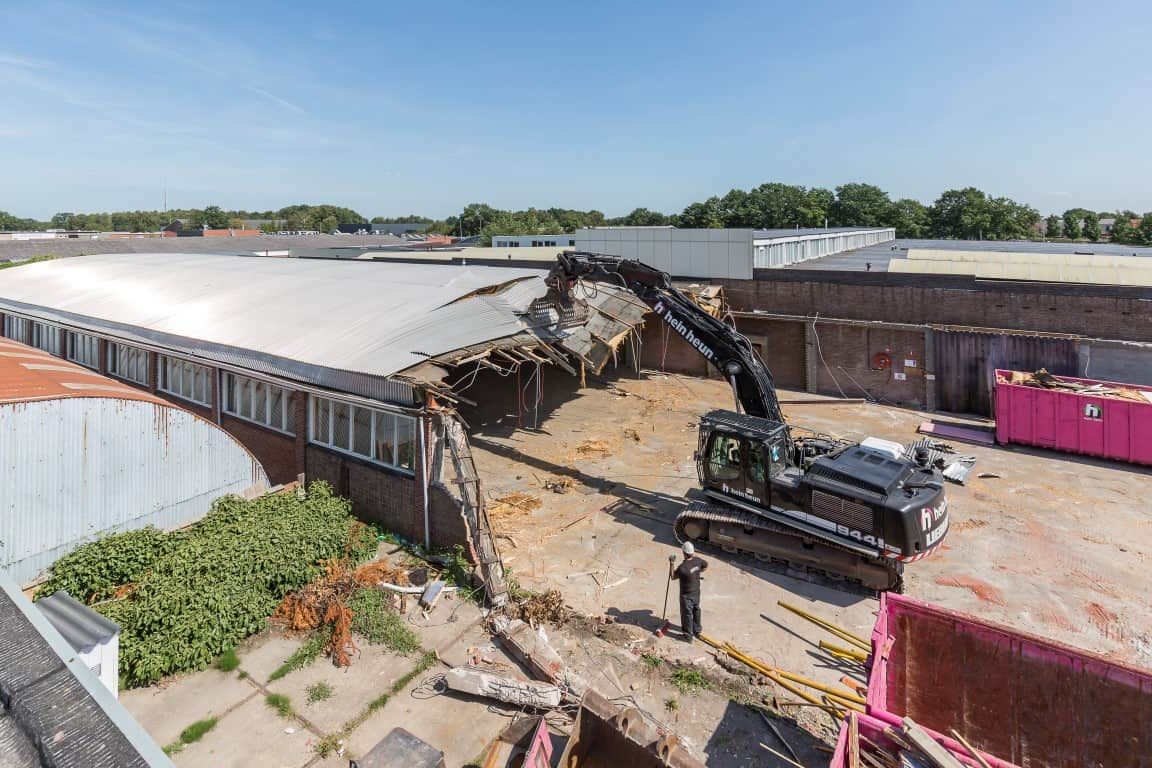 Bouwplaats met een kraan die een gebouw sloopt met roze containers