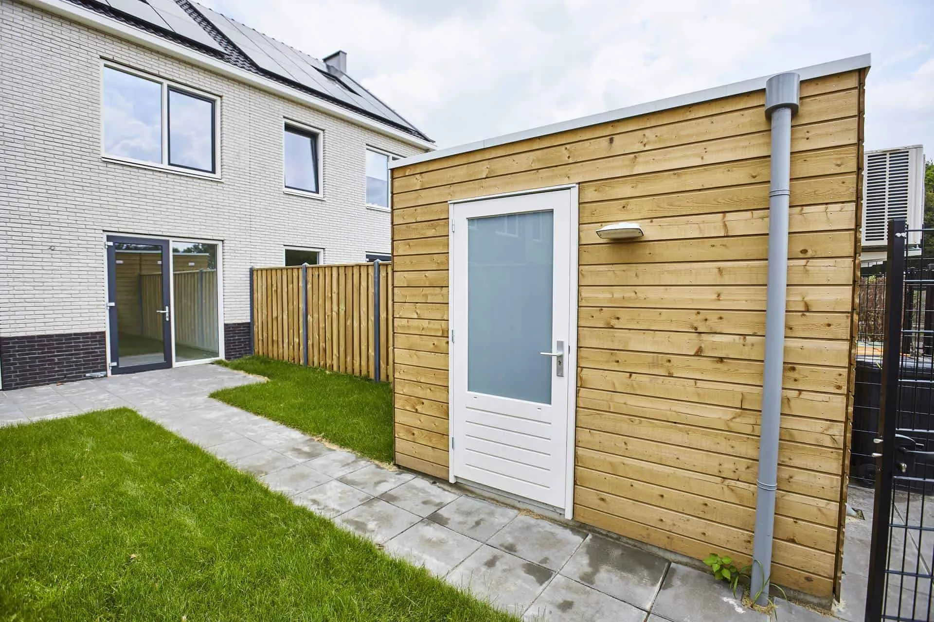 Gele berging met witte deur in tuin met gras