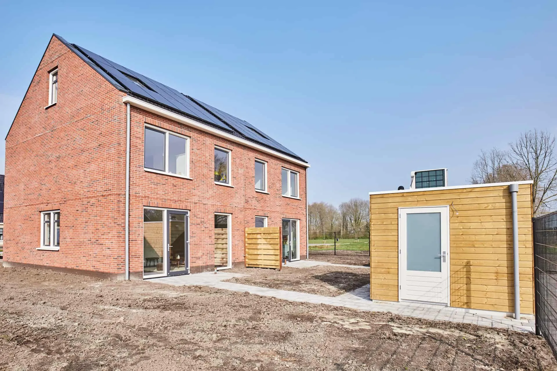 Nieuwbouwhuis met rode stenen en een gele houten berging in de achtertuin