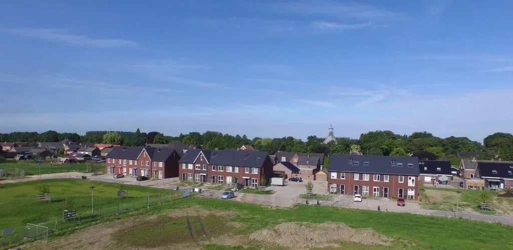 Vooraanzicht van nieuwbouw wijk met blauwe lucht en groen gras op de voorgrond