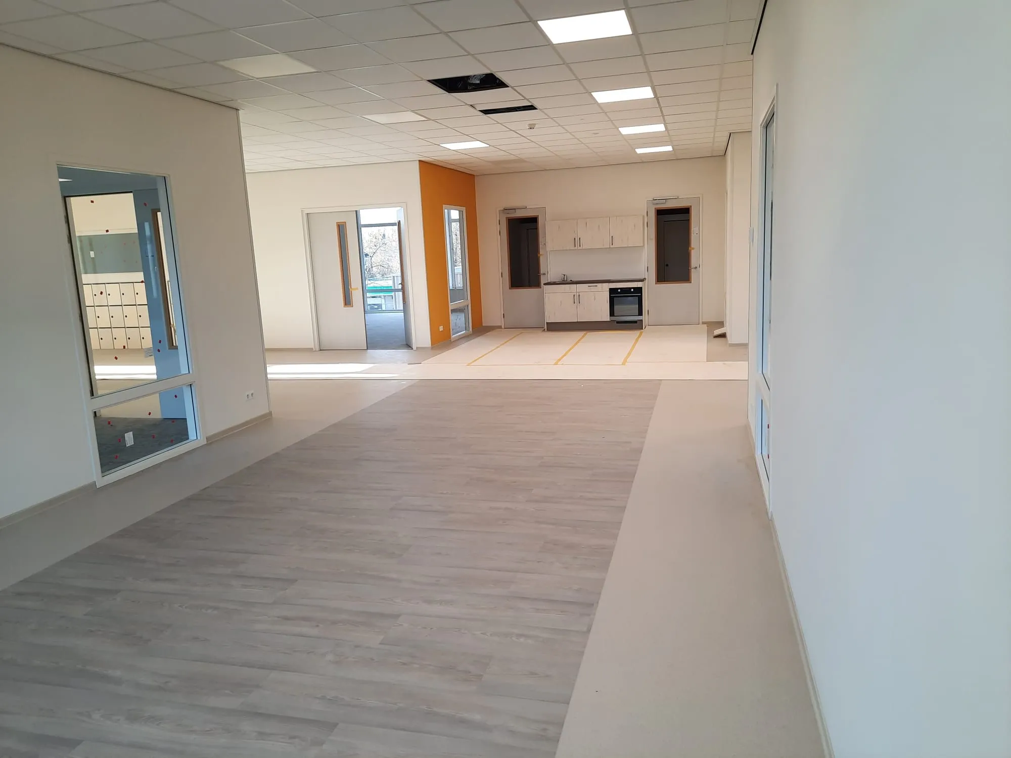 Witte binnenkant met ene oranje muur van een gebouw met een houten vloer en een keuken aan de achterwand