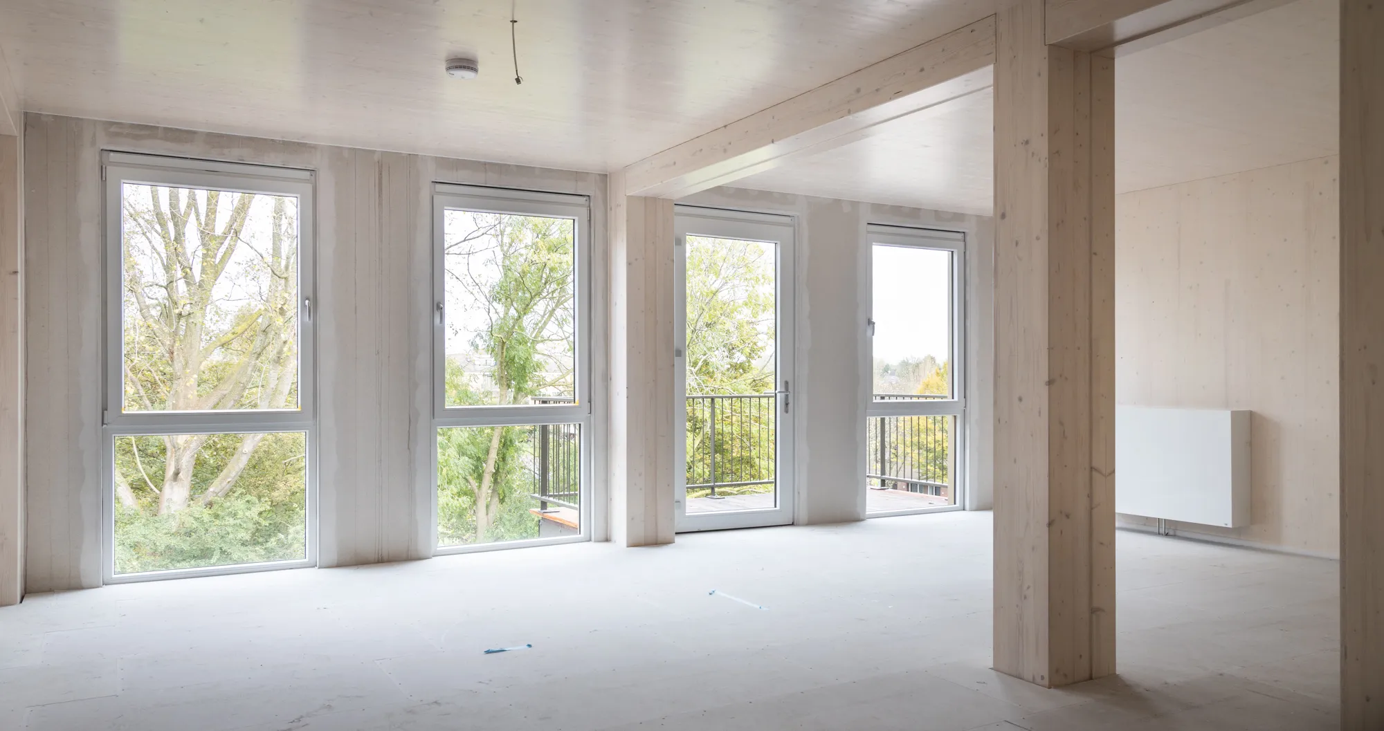 Binnenkant van een leeg appartement met balkon, houten balken en uitzicht op bomen