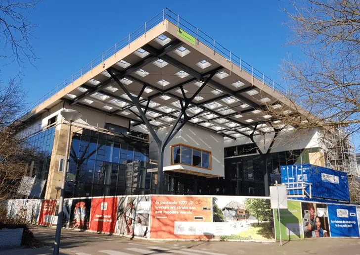 Glazen gebouw van voren met overkapping in aanbouw van hout met vierkante gaten in het dak