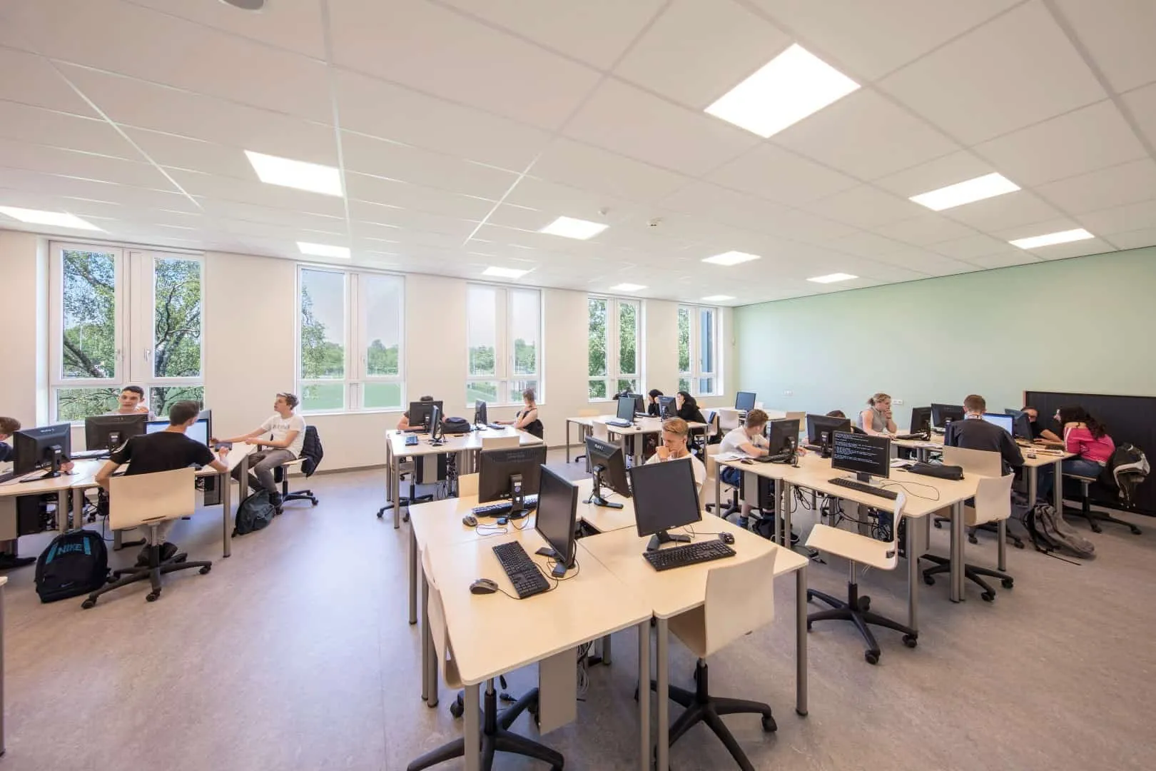 Computerlokaal met een groene muur en licht meubilair en leerlingen
