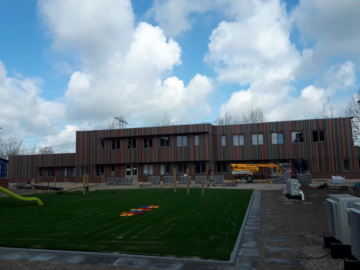 Rechthoekig gebouw met bruin en rode strepen met een grasveld ervoor