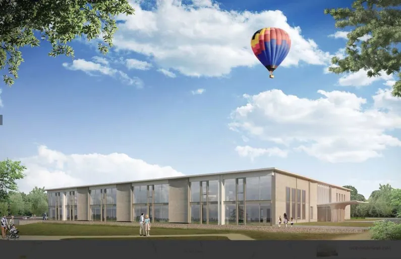 Laag gebouw met grote ramen op een grasveld met een luchtballon in de lucht