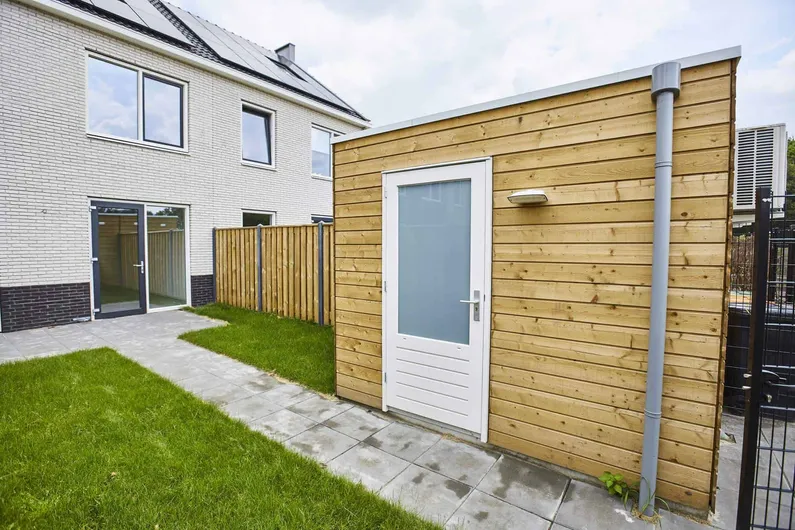 Gele berging met witte deur in tuin met gras