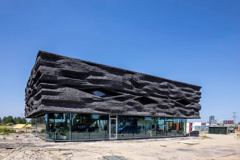 Stenen zwart gebouw met veel glas onderaan op zand