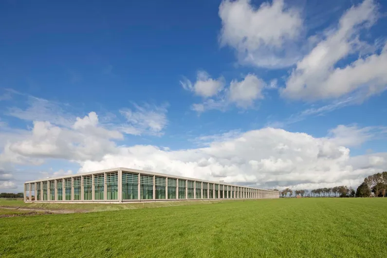 Houten gebouw met veel ramen van veraf met een grasveld ervoor