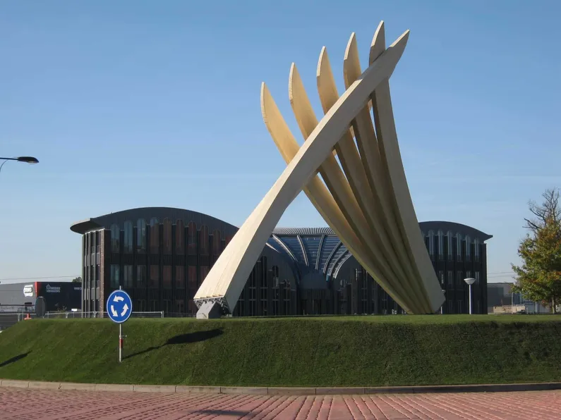 Kunstwerk van houten balken in elkaar verweven op een rotonde met gras erop