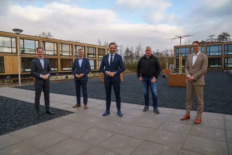 Minister Hugo de Jonge samen met vier andere mannen voor houten gebouwen met grote ramen