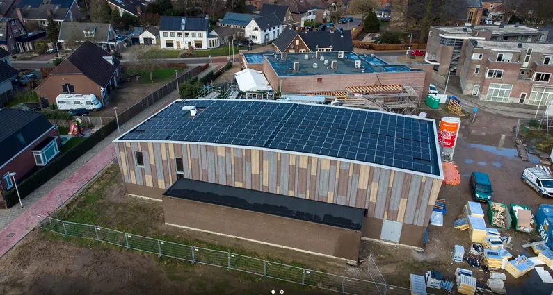 Gebouw met verschillende kleuren hout en zonnepanelen op het dak in een woonwijk